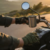A rider wearing Tactical-Style Fingerless Utility Gloves holds a coffee mug on a motorcycle, enjoying a scenic view.