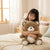 Soft Plush Teddy Bear Toy with Neck Pendant being hugged by a girl on a cozy bed in a bright room.