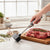 Meat Tenderizer Hammer being used on fresh meat with herbs and spices in a bright kitchen setting.